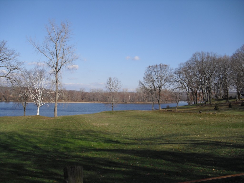 Manicured bank of river in winter - leafless trees frame ribbon of blue river. Connecticut River, Portland, CT