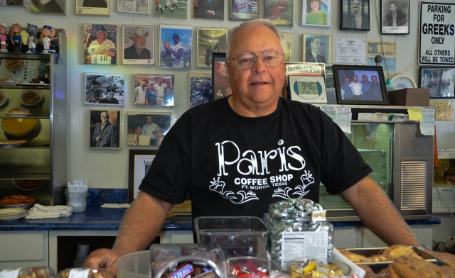 Mike Smith, owner of Paris Coffee Shop, posing with collection of memorabilia displayed on wall and on shelves.