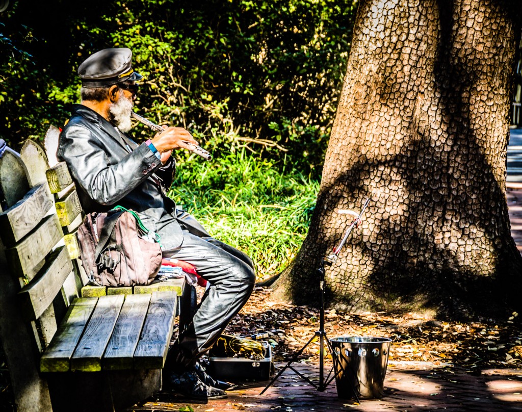 Man playing a flute, sitting on park bench at Johnson Square in Savannah, Georgia.