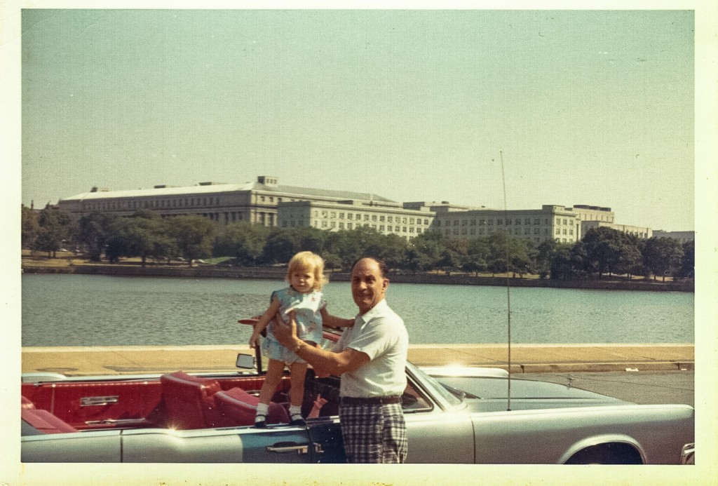 Grandfather holds up toddler Sandra Foyt on Lincoln Continental in Washington DC sometime in the early 1960s.