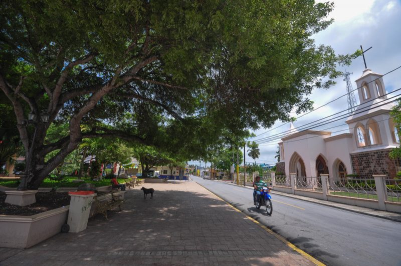 Motorcyclists passes the church and a dog in the town square in Cabrera, Dominican Republic.