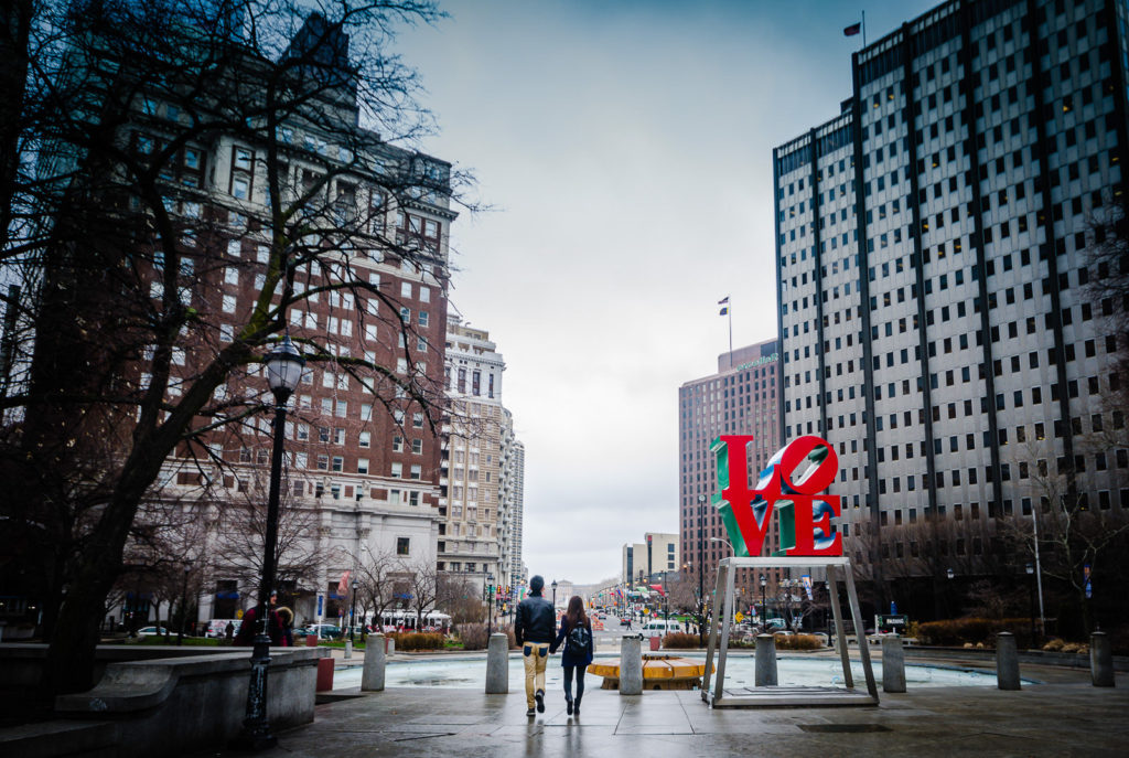 Couple walks holding hands past the Philadelphia Love Sign.