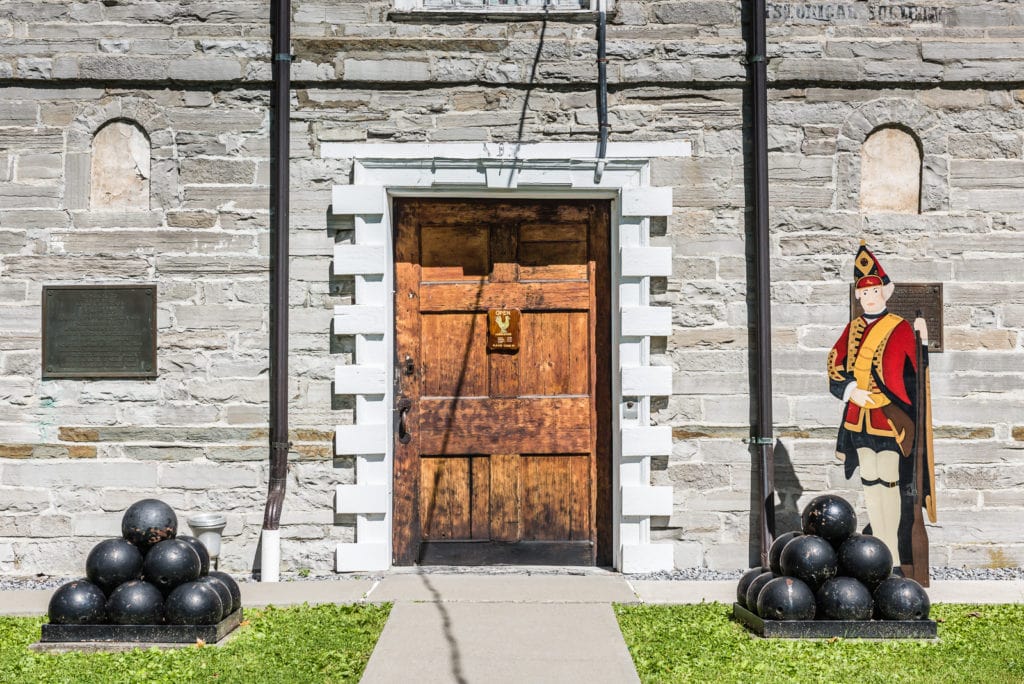 Front entrance of Old Stone Fort Museum in Schoharie, New York. A pile of cannon balls and wooden cutout soldier are posted at the door.