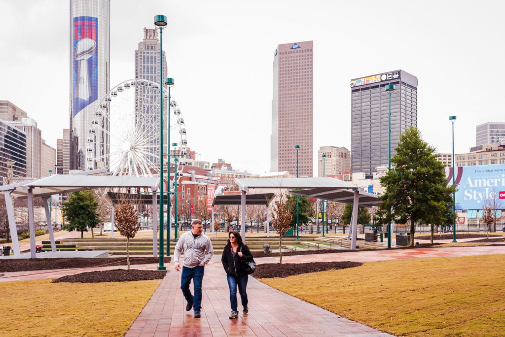 Couple walks in Centennial Olympic Park with city skyline in background.