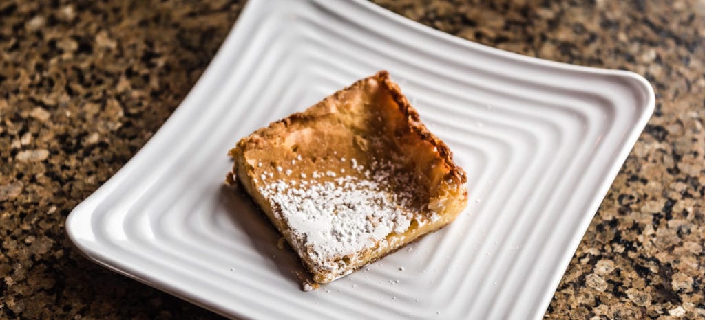 Square of Gooey Butter Cake with powdered sugar sprinkled on top served on white plate at Parker Coffee in St. Louis MO.