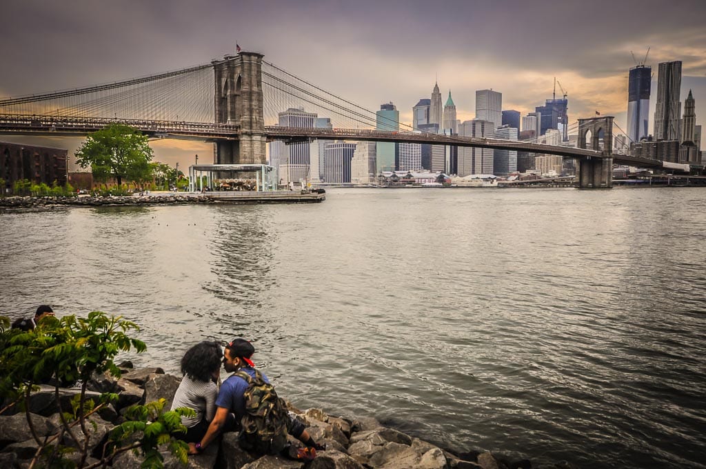 Couple smooches in front of sunset view of the Brooklyn Bridge.