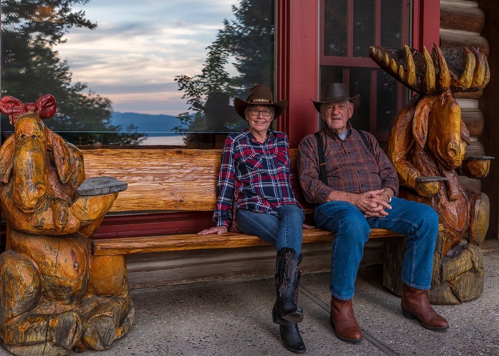 Western couple sits on carved wooden bench at Flathead Lake Lodge.