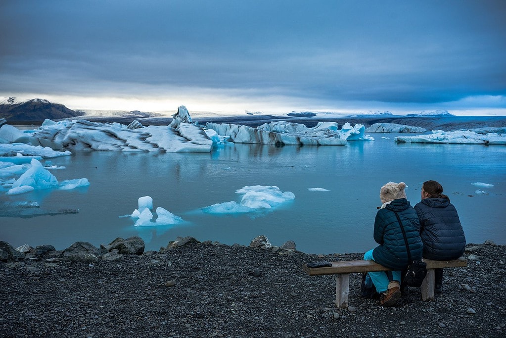 Couple sits on the shore of the Jokulsarlon Glacier Lagoon.