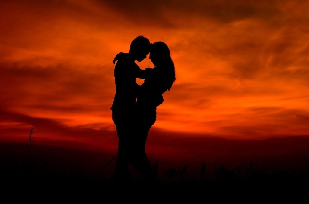 Silhouetted couple embraces against red sky on romantic getaways in USA.