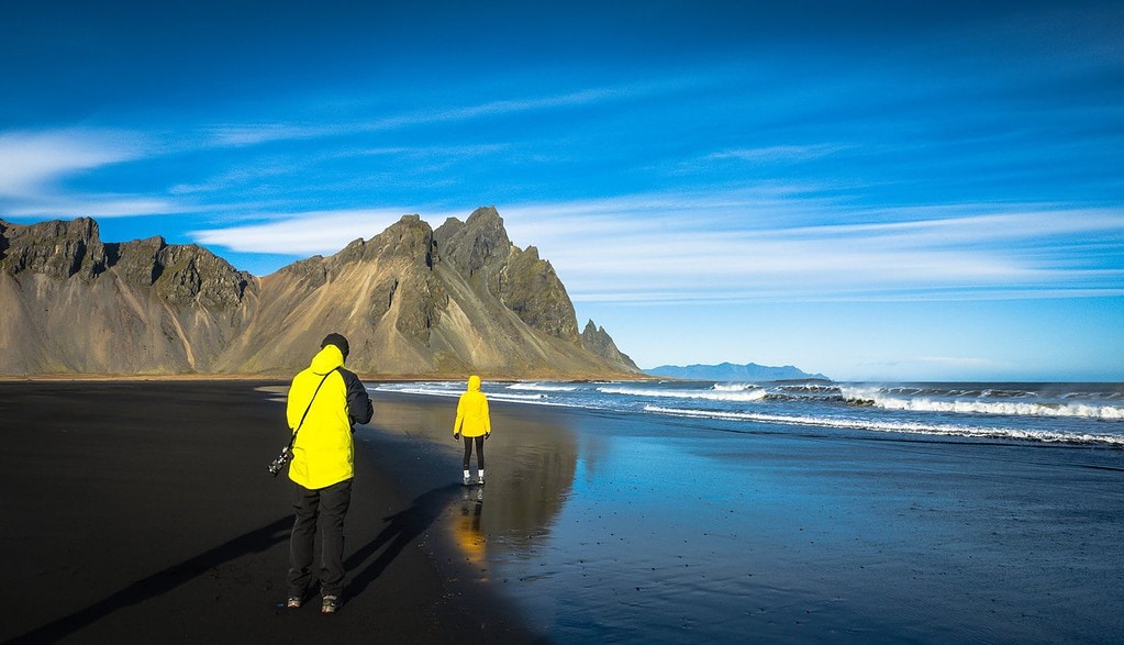 Couple wears rain jackets - an essential item on the Iceland packing list - at Vestrahorn shore.