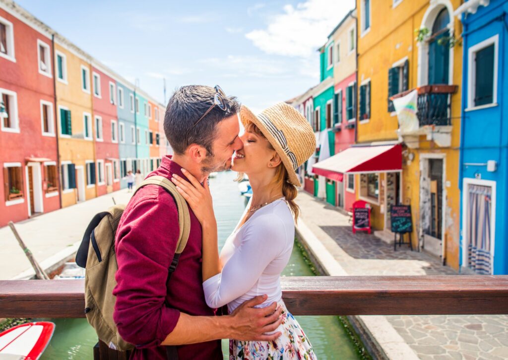 Couple kisses in front of colorful buildings in a romantic destination.