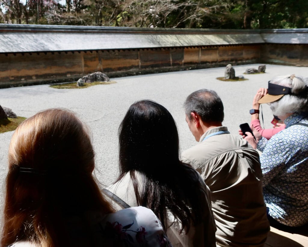 Zen peaceful visitors meditating at rock garden at Ryoan Ji Temple in Kyoto Japan